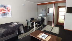 A compact hotel room with a sofa, a small dining table, a coffee table, and a kitchenette. - Anchor Motel (Timaru)