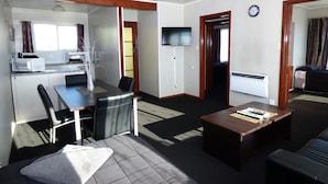 A compact living space with a kitchenette, a dining area, a seating area with a coffee table, and a television. - Anchor Motel (Timaru)