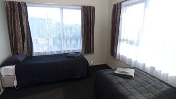 A hotel room with two beds, a window with curtains, a small bedside table, and a power outlet.