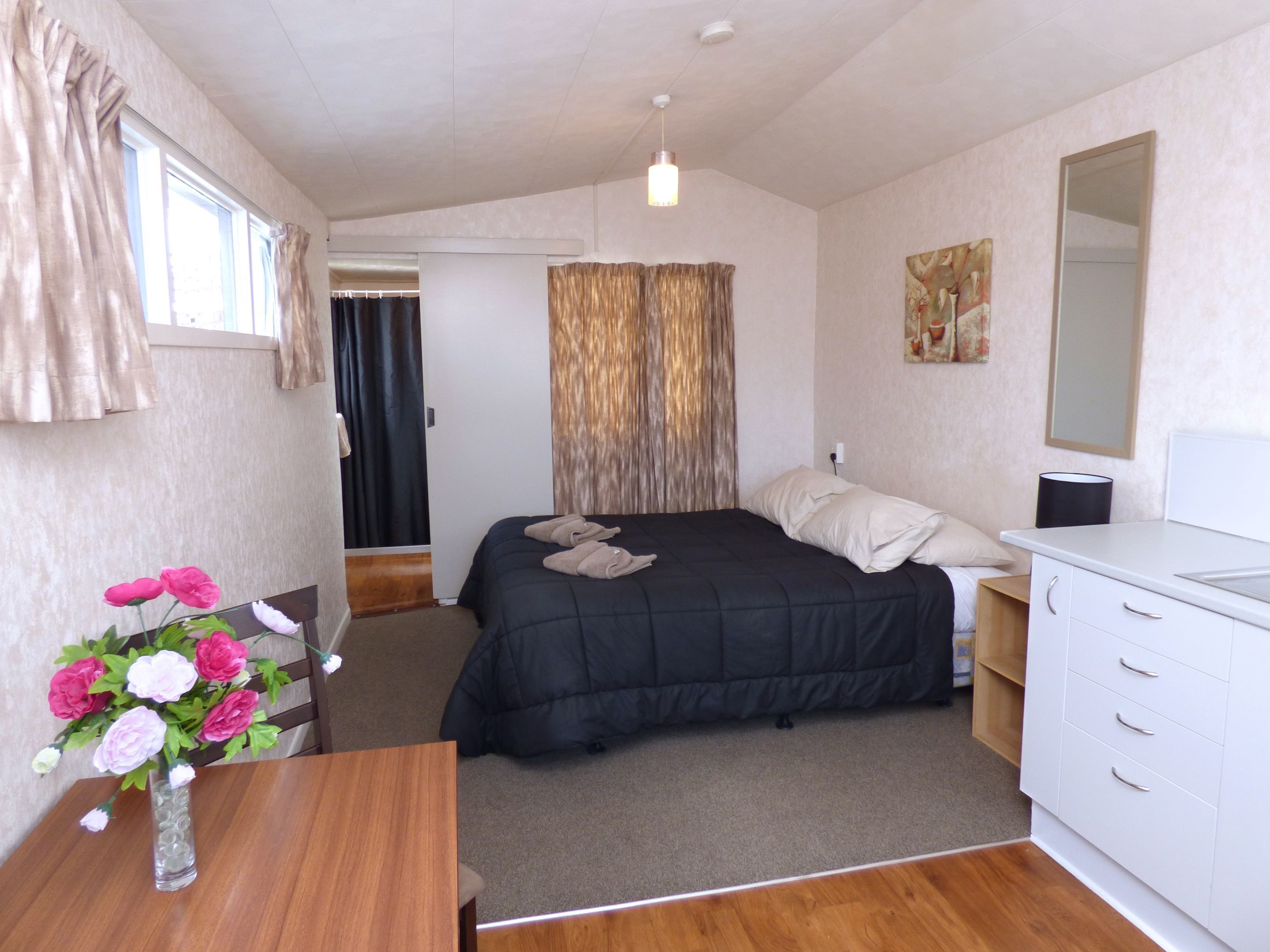 A bedroom with a bed, a dresser, a mirror, and a vase with flowers.