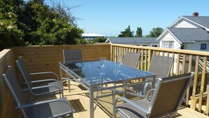 An outdoor deck with a glass-top table and metal chairs, surrounded by a wooden fence. - Anchor Motel (Timaru)