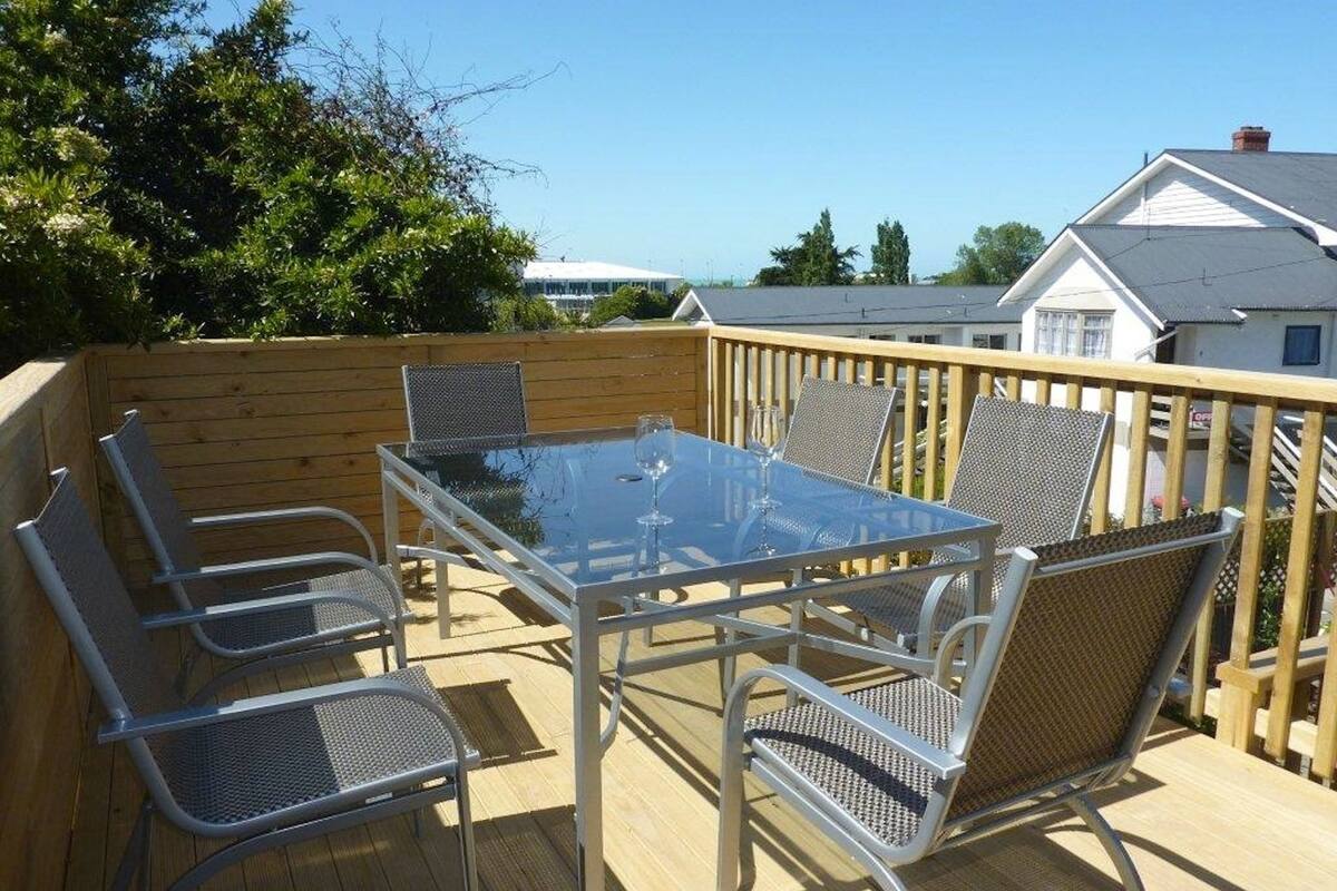 An outdoor deck with a glass-top table and metal chairs, surrounded by a wooden fence.