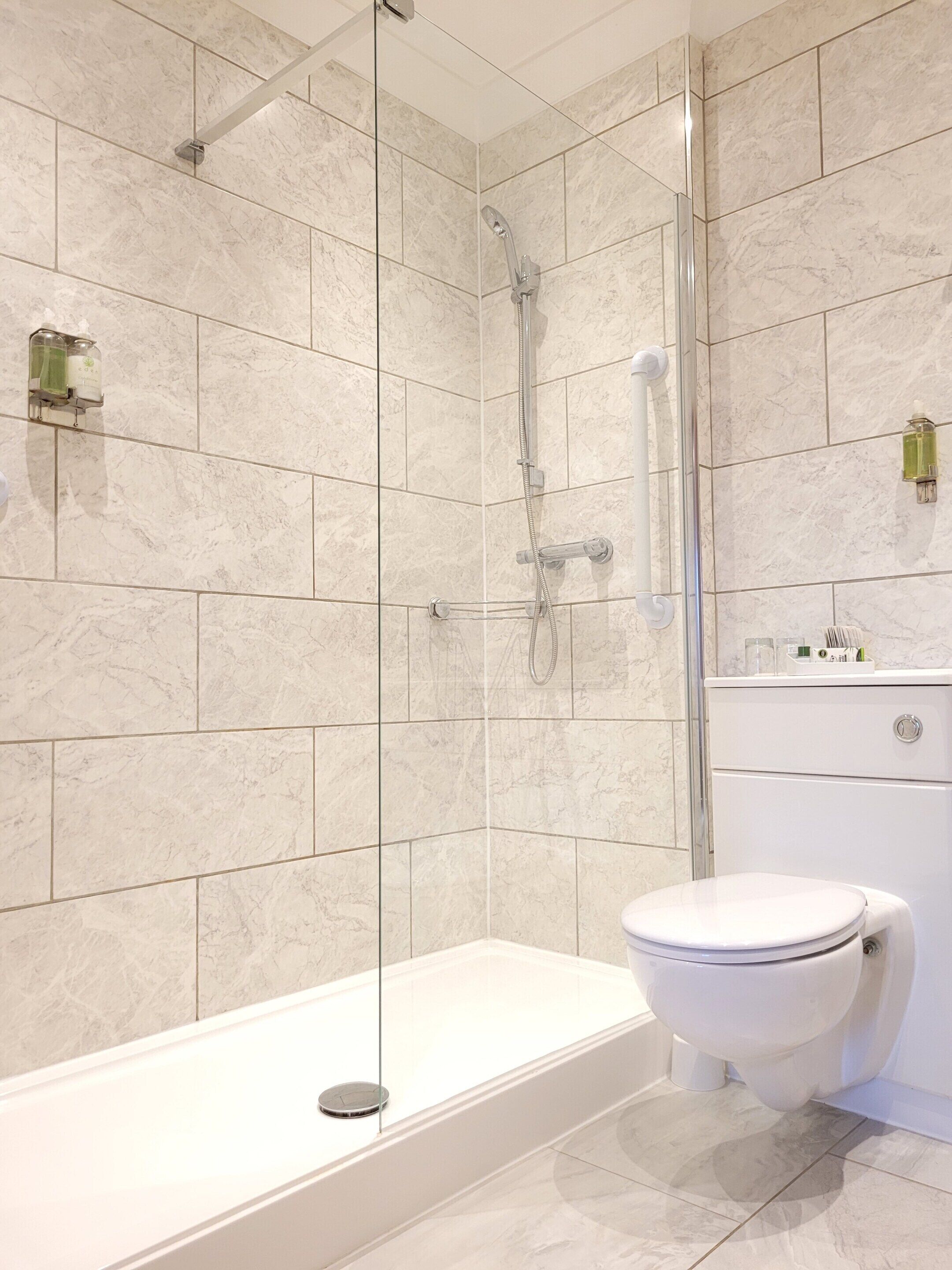 A modern bathroom with a glass-enclosed shower, a white bathtub, and a toilet.