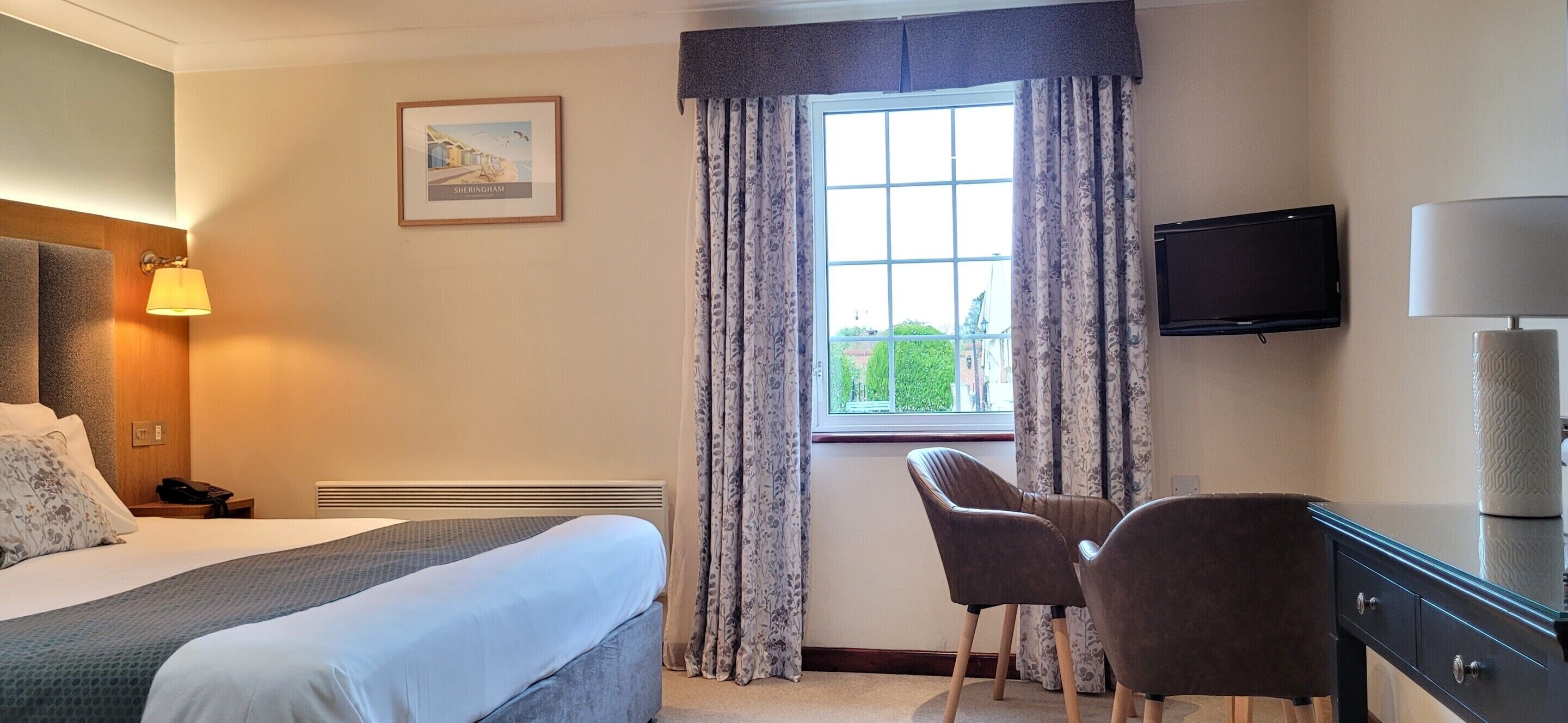 A hotel room with a bed, a desk, a chair, a television, and a window with curtains.
