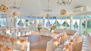 Een bruiloftlocatie met rijen witte stoelen, een middenpad en bloemendecoraties.