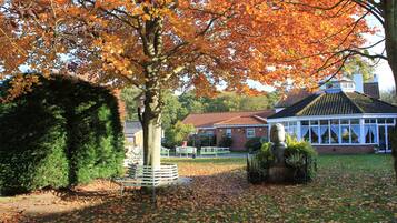 A park with a bench, a statue, and a building with a red roof.