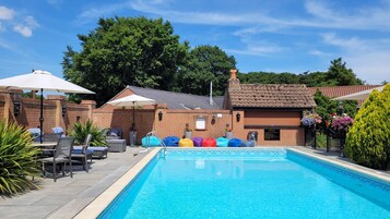 Piscina con sillas de descanso y sombrillas, rodeada de muros de ladrillo y follaje.