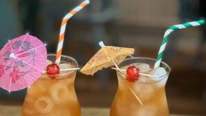Deux cocktails servis dans des verres à pied, avec des pailles et des petits parasols.