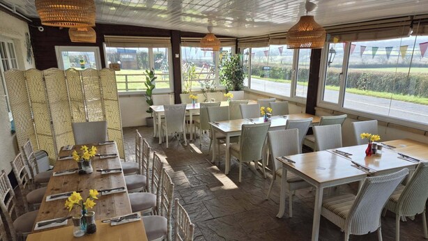 Un restaurant doté d'une terrasse, de chaises en osier et de tables décorées de fleurs jaunes.