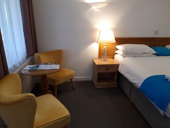 Una habitación de hotel con una cama, una mesita de noche con una lámpara, una silla y una pequeña mesa con folletos.