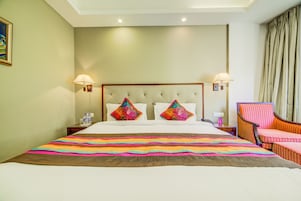 Habitación de hotel con una cama grande, dos almohadas decorativas, una silla a rayas y una mesita de noche con lámpara.