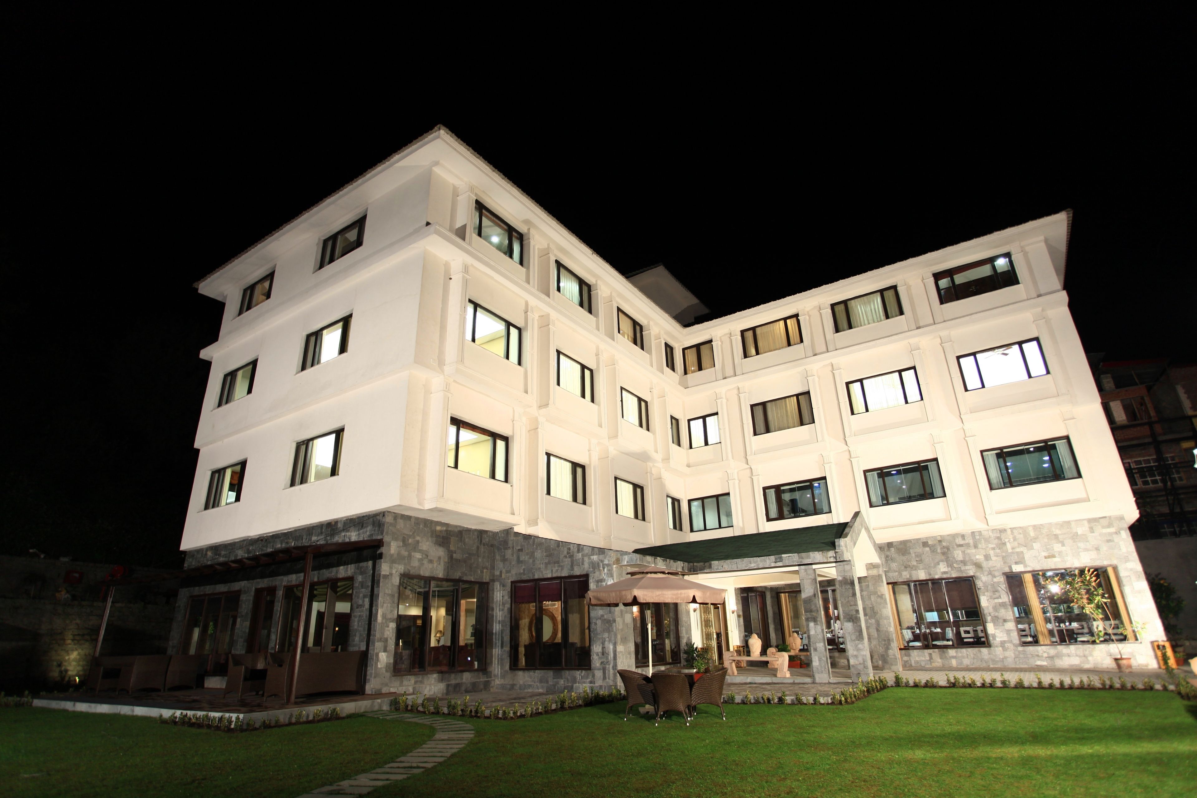 A multi-story hotel with a modern design, featuring a well-lit entrance and a patio area with outdoor seating.