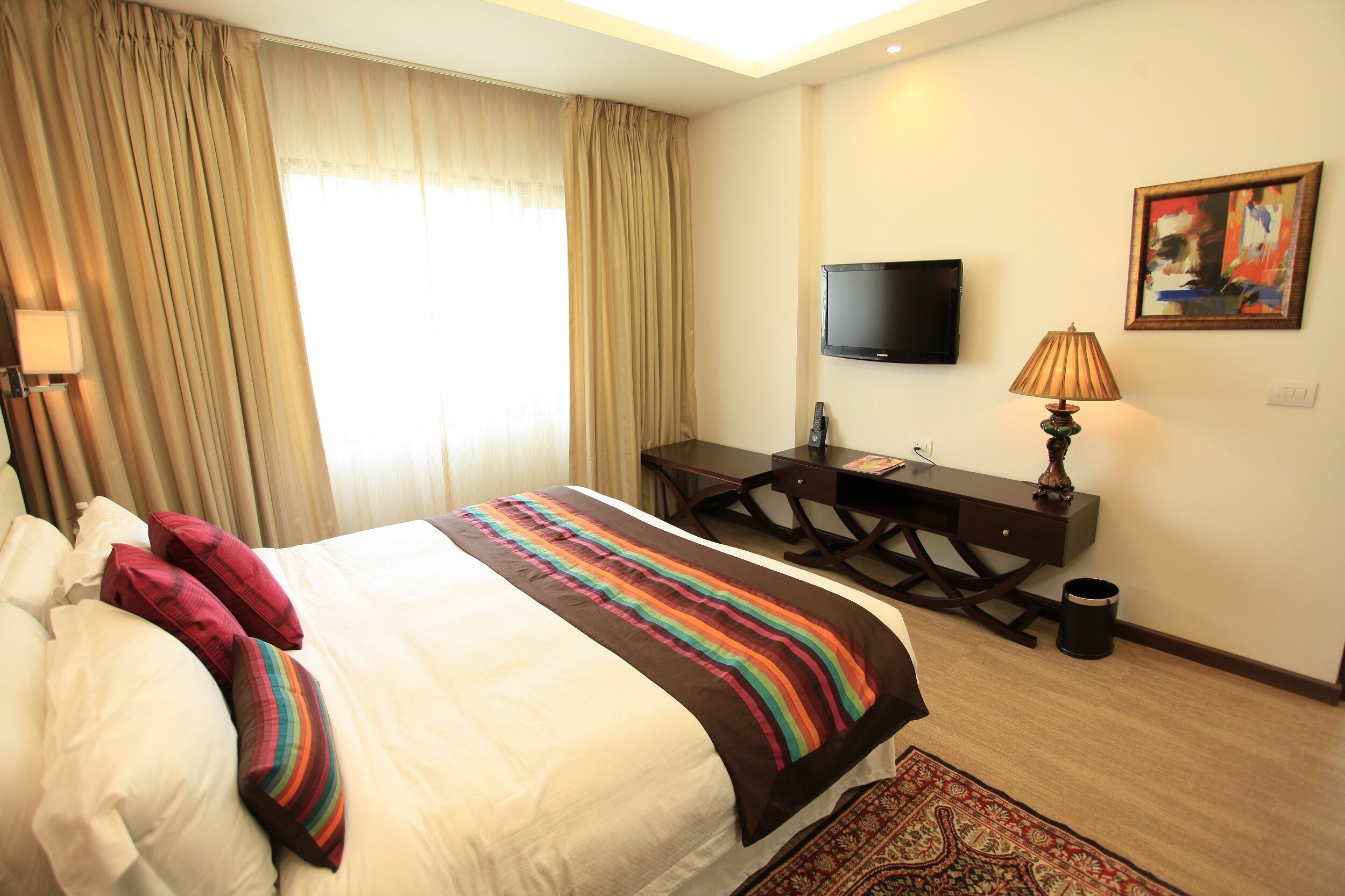 A hotel room with a bed, a desk, a television, and a painting on the wall.