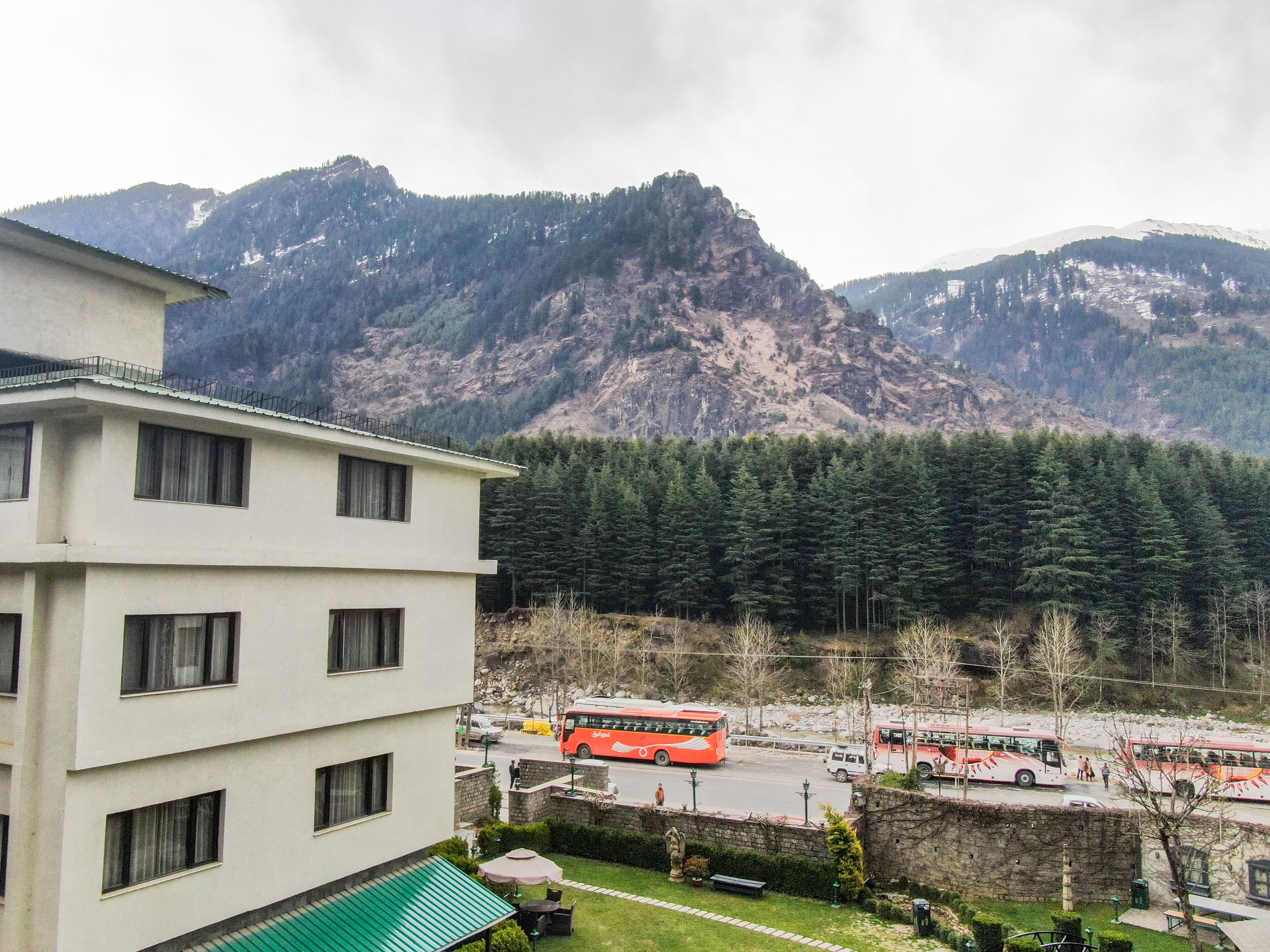 A multi-story building with a flat roof and a green awning, situated in a mountainous area with a view of dense forests and rocky mountains.