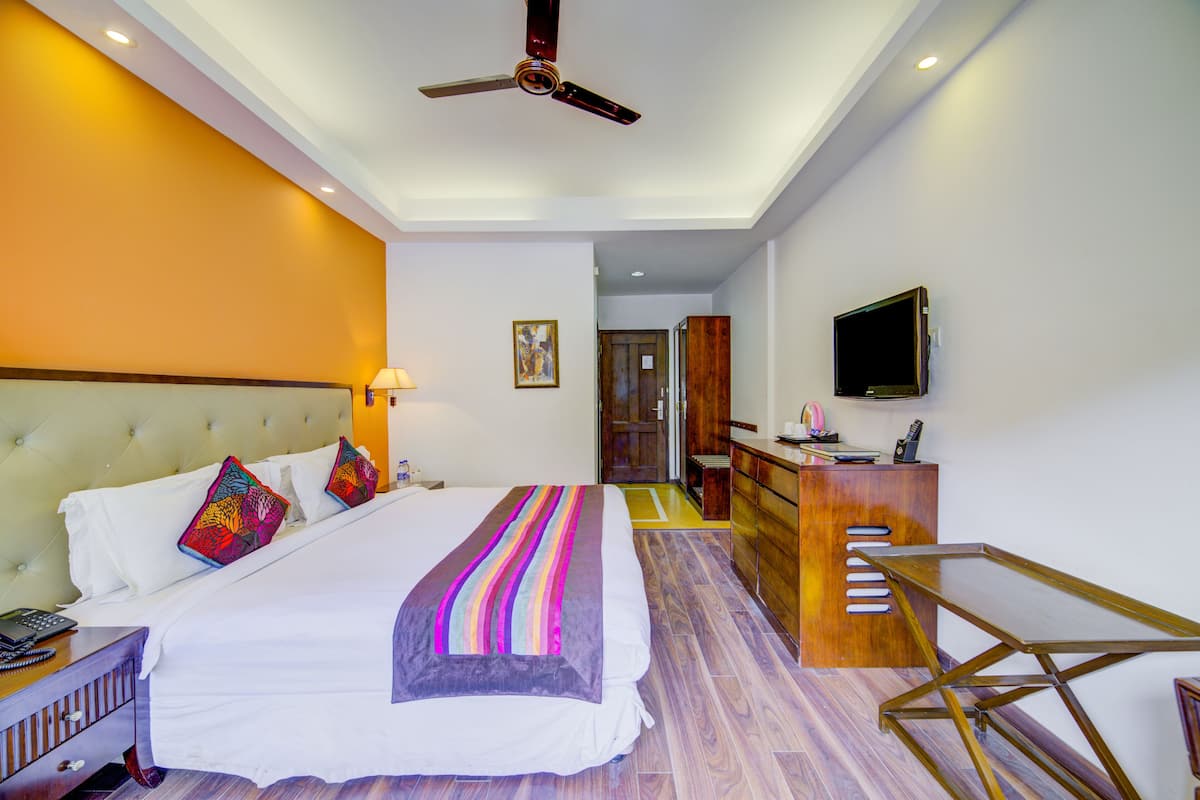 Une chambre d’hôtel équipée d’un lit, d’une table de chevet, d’un bureau, d’une chaise, d’une télévision et d’un ventilateur de plafond.