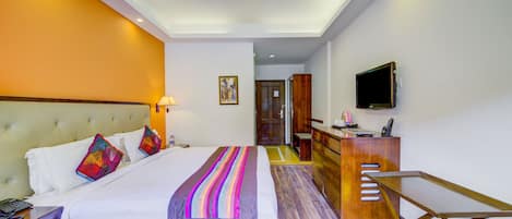 Habitación de hotel con cama, mesita de noche, escritorio, silla, televisor y ventilador de techo.