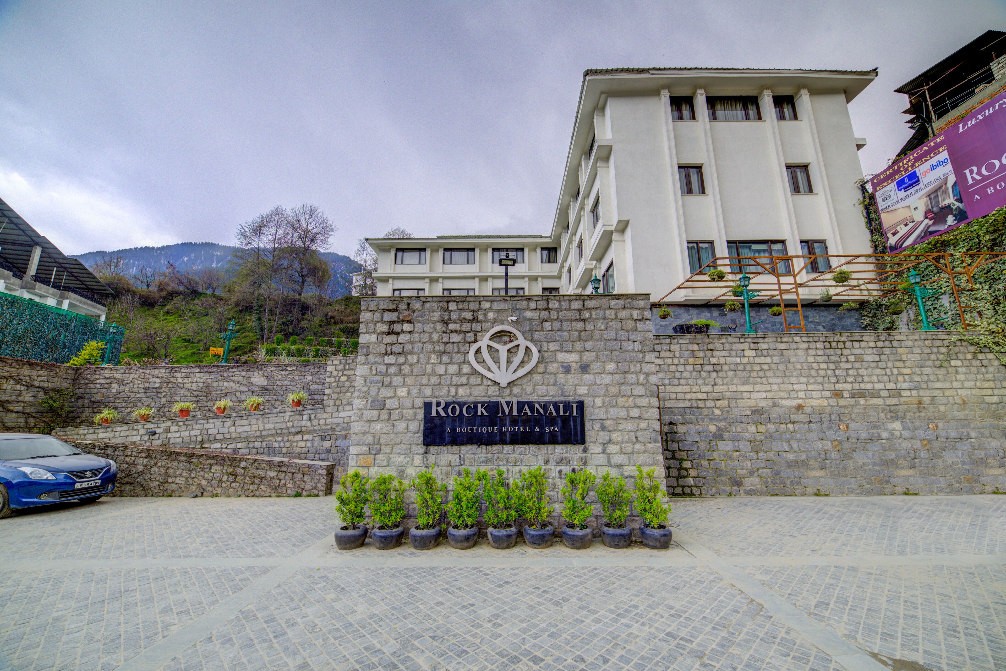 Letrero del Rock Manali Boutique Hotel & Spa, con una pared de piedra y plantas en macetas al frente.