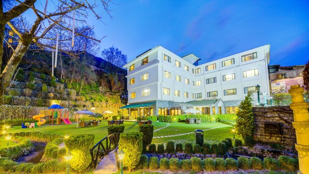 Ein modernes Hotel mit mehreren Etagen, einem gepflegten Garten mit Wegen und einem Spielbereich.