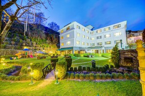 Ein modernes Hotel mit mehreren Etagen, einem gepflegten Garten mit Wegen und einem Spielbereich.