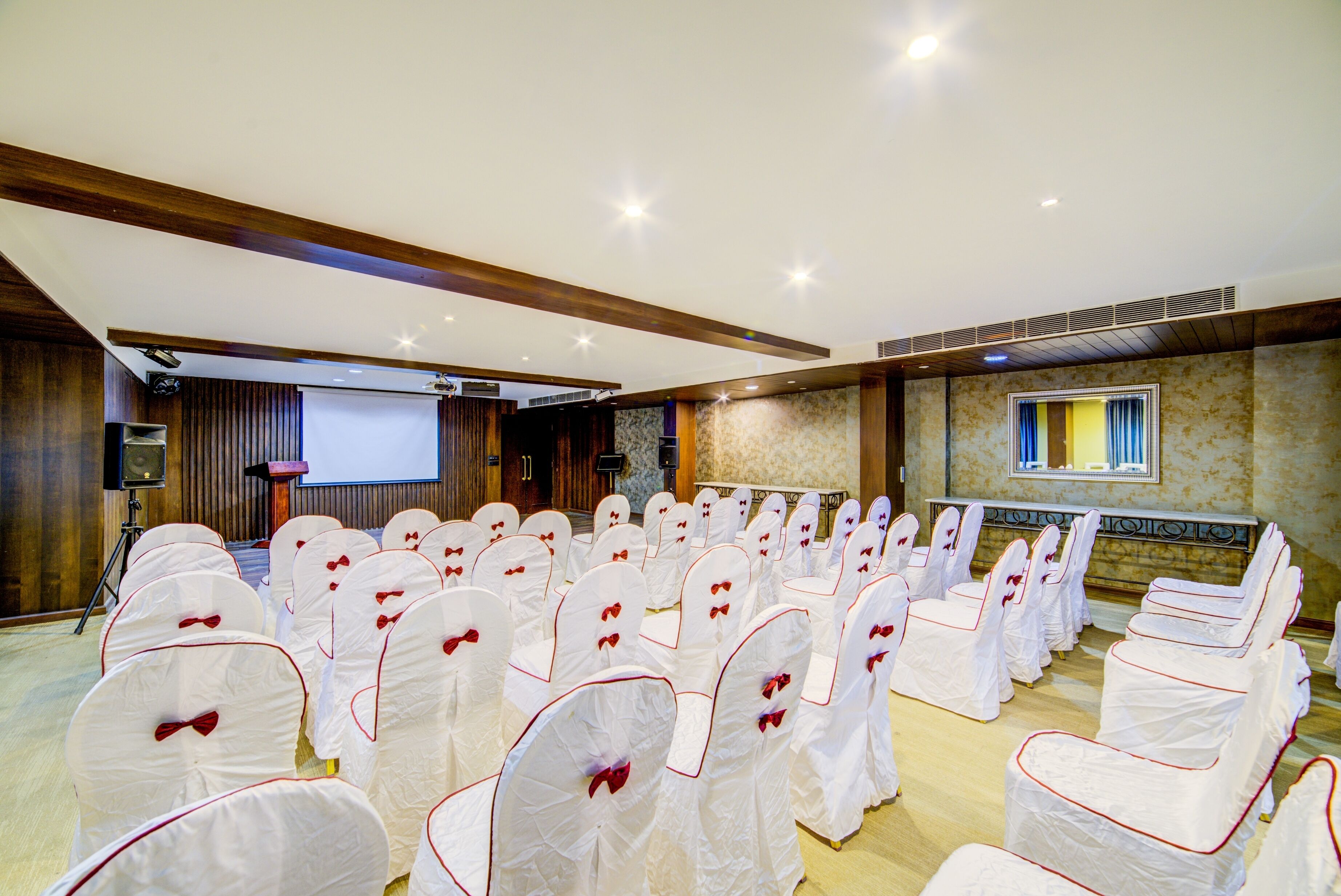 A conference room with rows of white chairs with red accents, a projector screen, and a presentation podium.