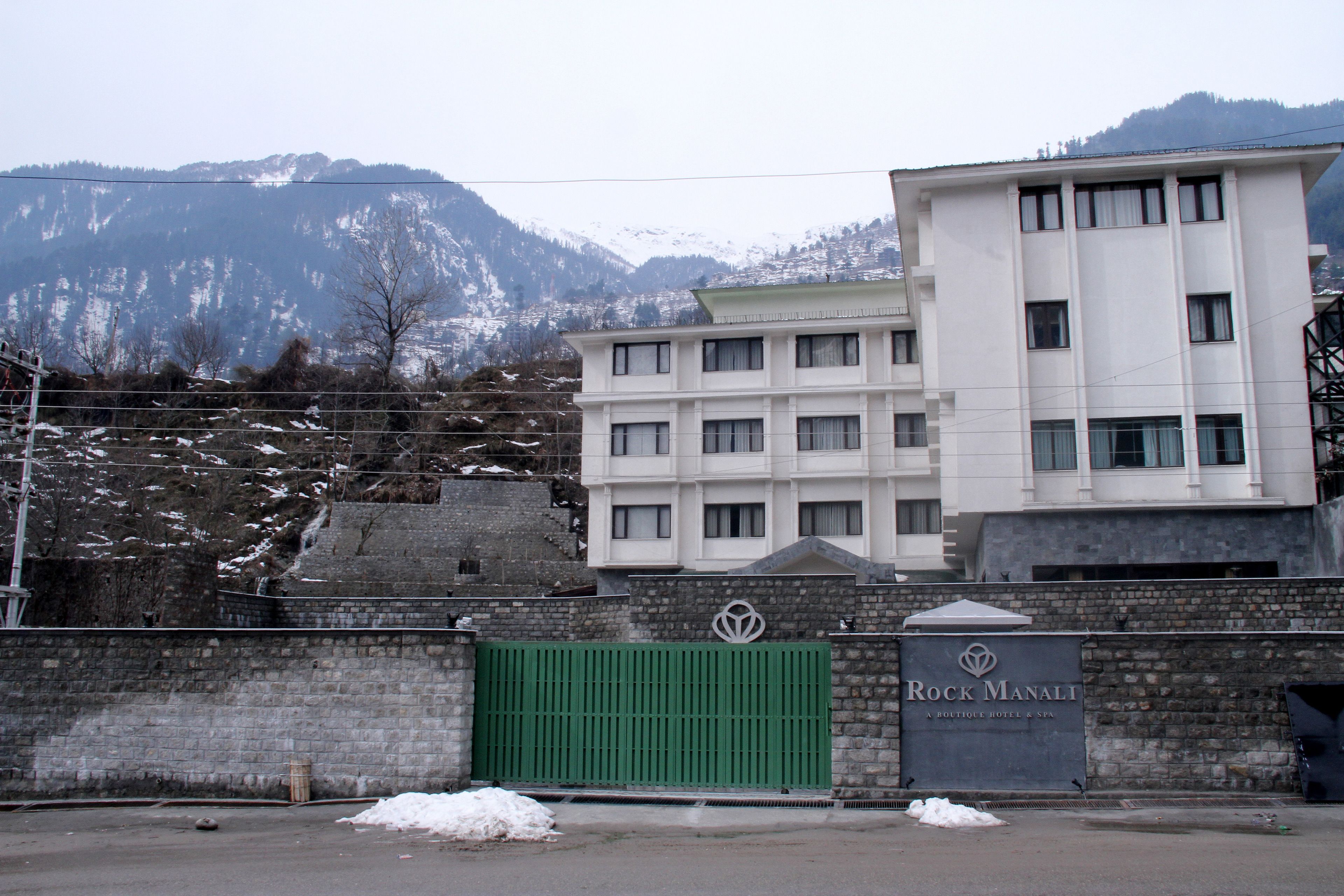 A hotel with a modern facade, a gated entrance, and a mountainous backdrop.