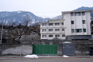 A hotel with a modern facade, a gated entrance, and a mountainous backdrop.