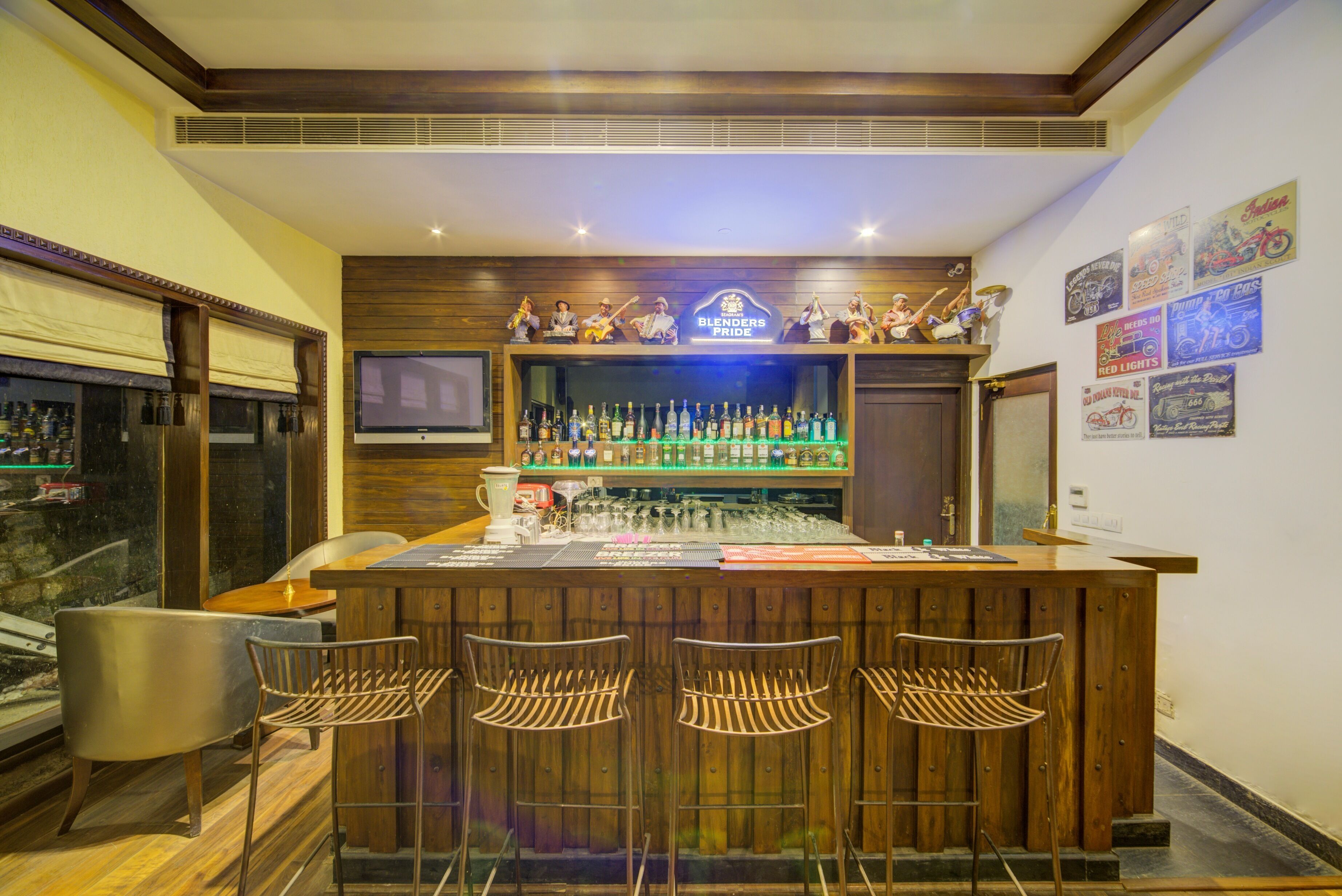 A bar area with a wooden counter, bar stools, a television, and a wall with various posters.
