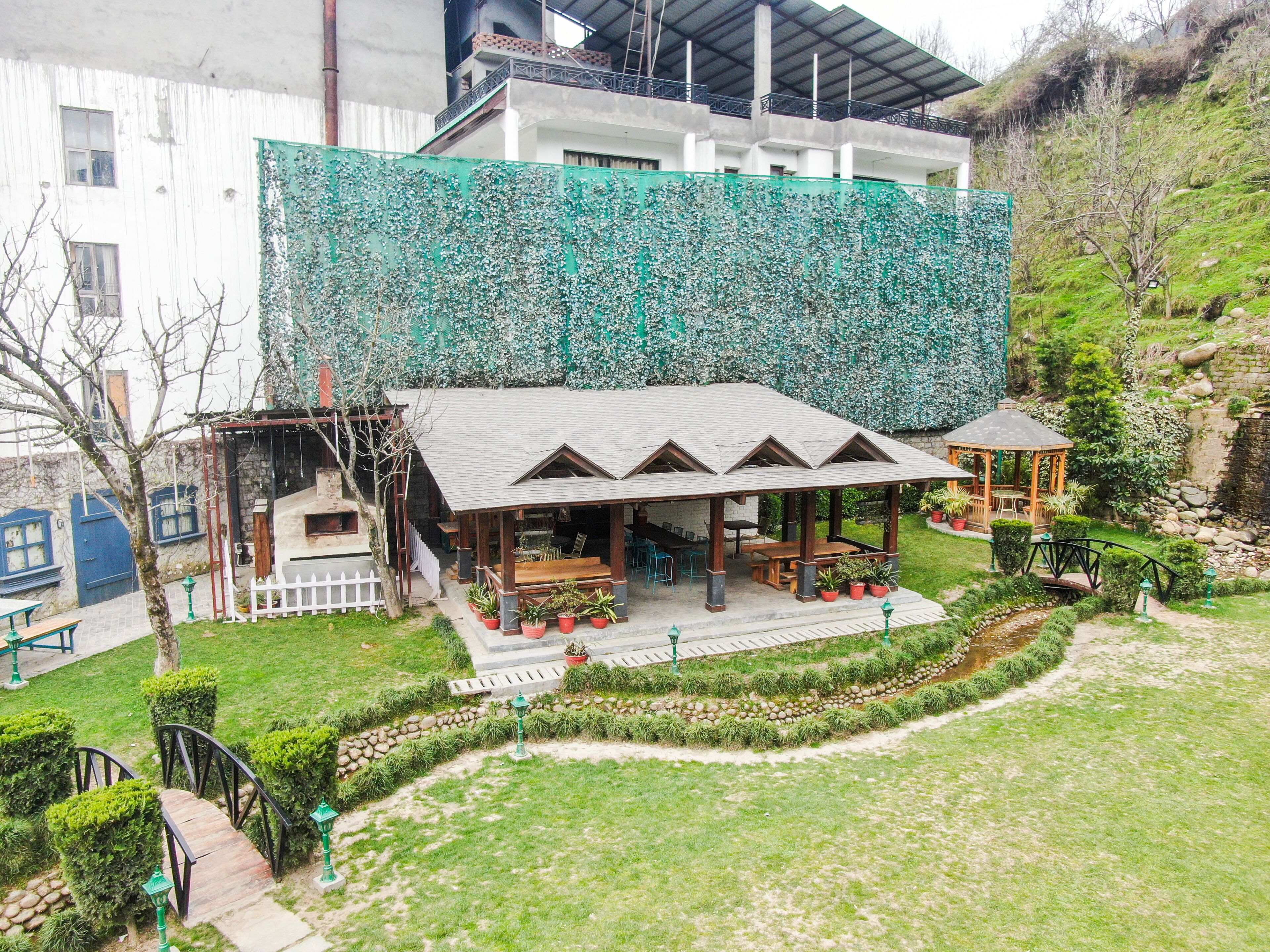 A building with a green ivy-covered wall, a covered outdoor seating area with tables and chairs, and a small gazebo.