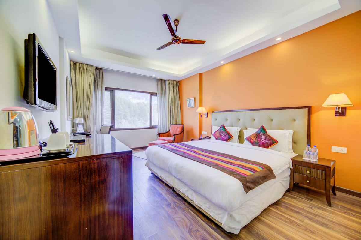 Une chambre d’hôtel avec un grand lit, un bureau, une télévision, un ventilateur de plafond et une fenêtre avec des rideaux.