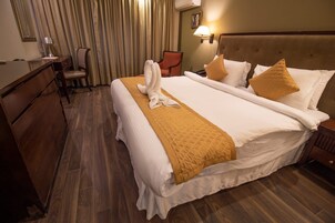 Quarto de hotel com uma cama grande, uma mesa, uma cadeira e uma mesinha de cabeceira.