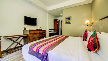 A hotel room with a bed, a desk, a television, and a bathroom visible through an open door.