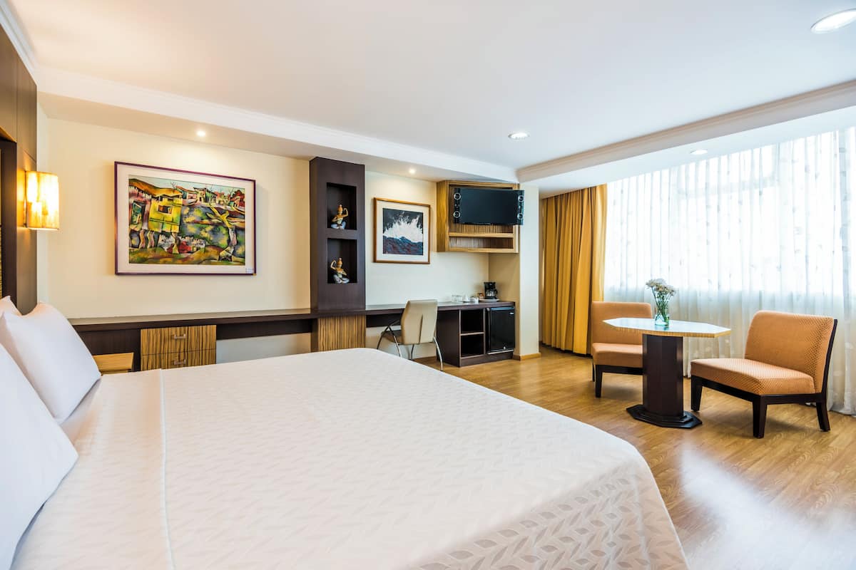Een hotelkamer met een groot bed, een bureau met een computer, een televisie en een zithoek met stoelen.