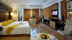 Een hotelkamer met een bed, een eettafel met een fruitschaal, een televisie en een beeld.