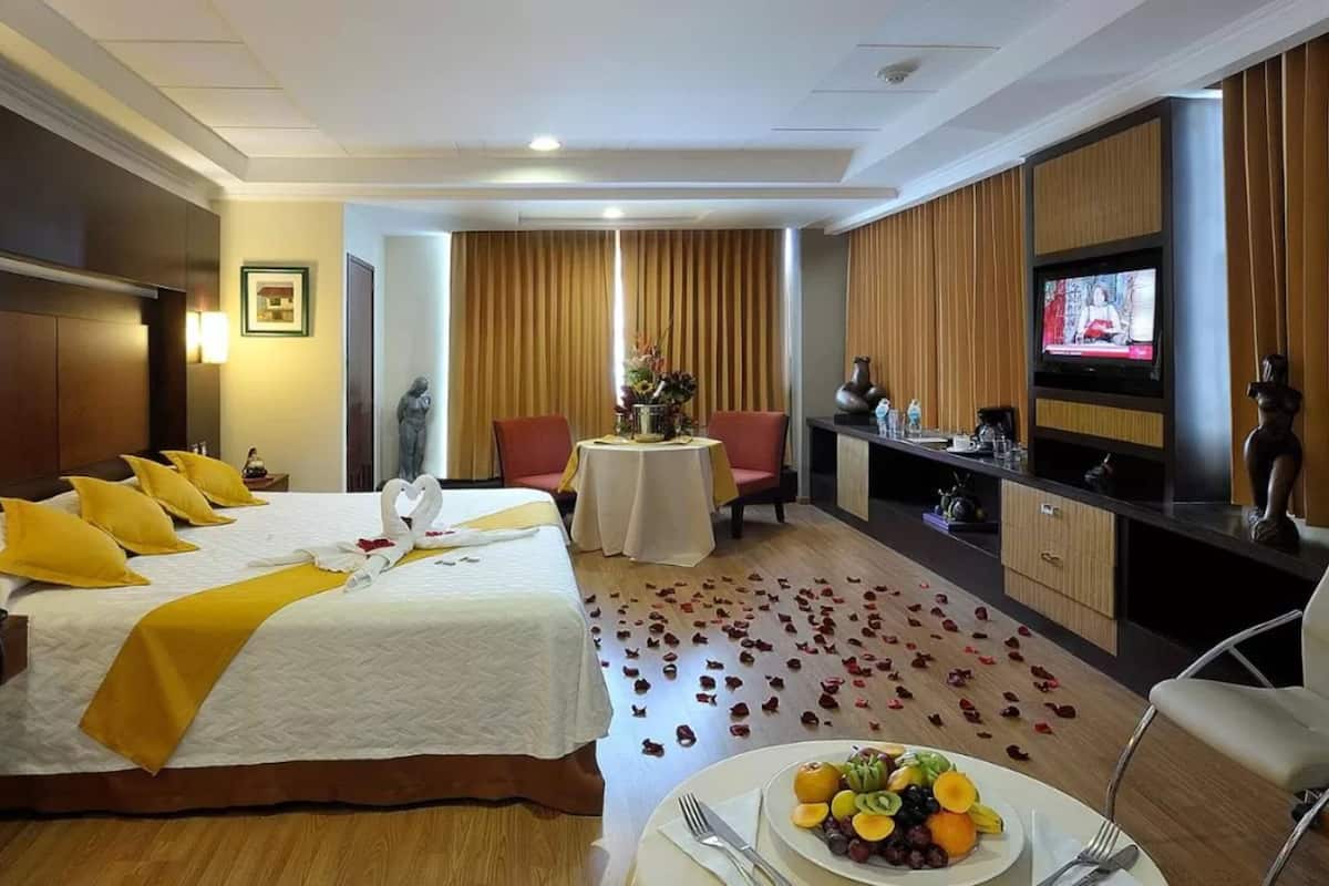 Een hotelkamer met een bed, een eettafel met een fruitschaal, een televisie en een beeld.