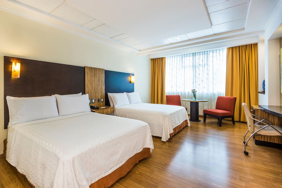 Een hotelkamer met twee bedden, een bureau, een stoel en een kleine tafel met een bloevas.
