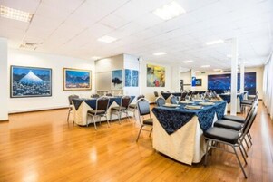 Un salón de conferencias con varias mesas y sillas, paredes blancas y obras de arte enmarcadas.