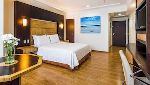 Een hotelkamer met een bed, nachtkastje en een schilderij van een strandgezicht.