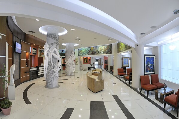A spacious lobby with a high ceiling, modern seating areas, and a large mural on the wall. - Hotel GH Galeria (Guayaquil)
