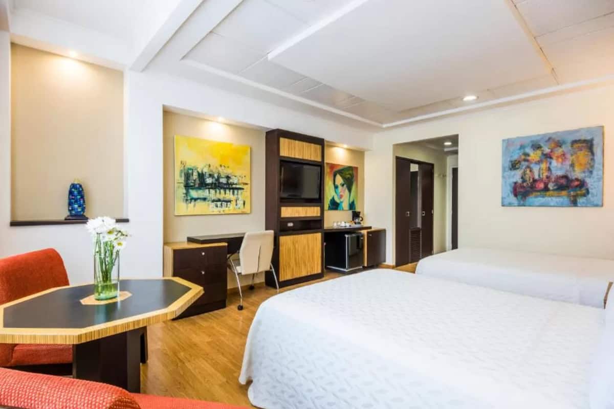 Een hotelkamer met een bed, een bureau met stoel, een televisie en kunstwerken aan de muur.