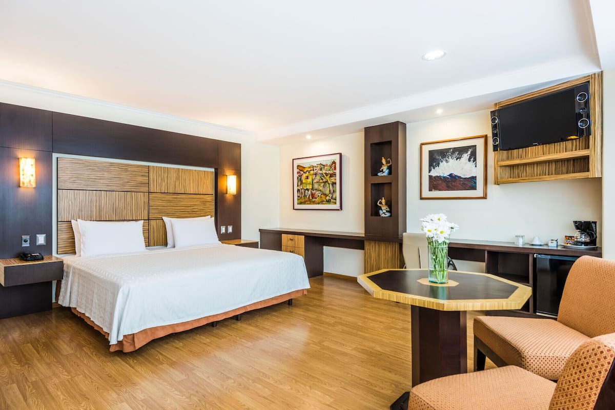 Een hotelkamer met een groot bed, een bureau met stoel, een televisie en kunst aan de muren.