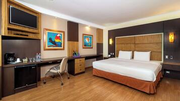 Quarto de hotel com uma cama grande, uma mesa com cadeira, televisão e obras de arte nas paredes.