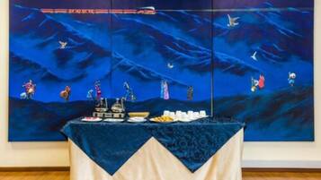 Una habitación con un cuadro grande que muestra un paisaje marino azul en la pared, una mesa con mantel y varios objetos sobre ella.