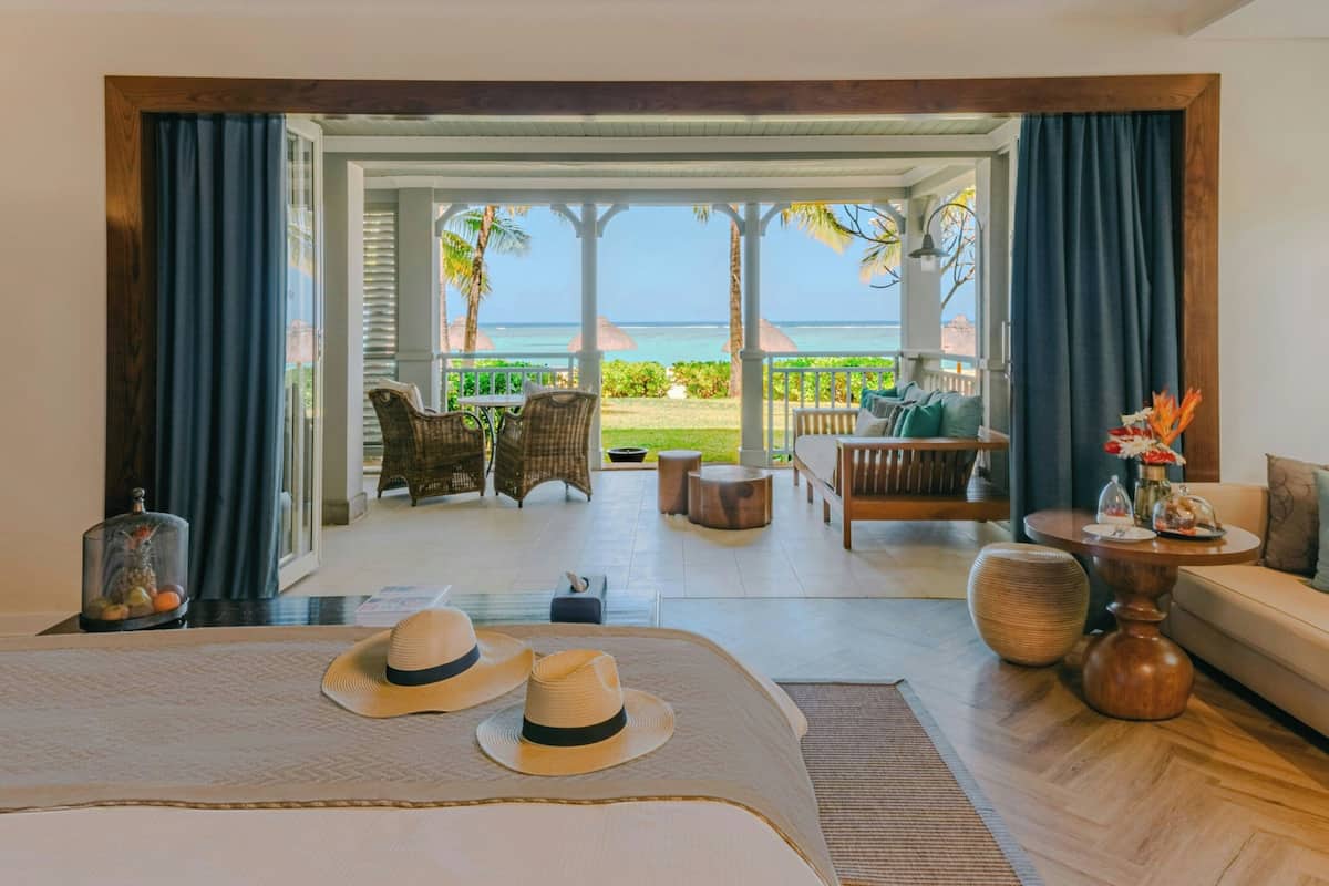 A hotel room with a large bed, a view of the ocean, and a balcony with outdoor furniture.