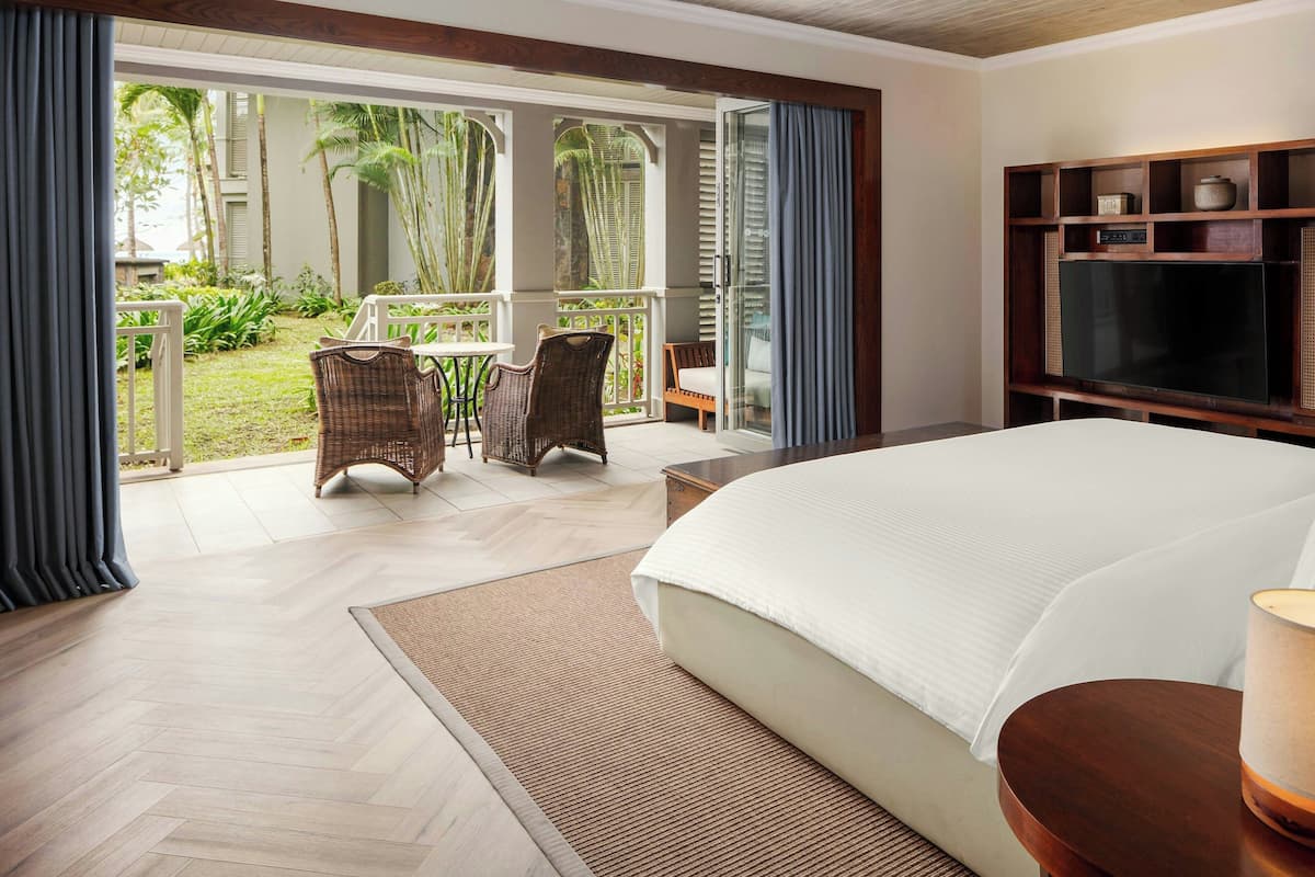 A bedroom with a large bed, a TV, and a view of a garden through a sliding door.