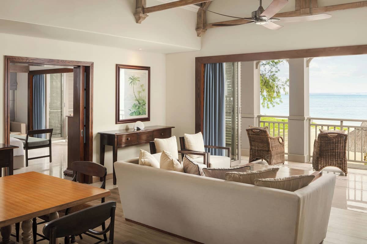 A spacious living area with a wooden dining table, a sofa with cushions, wicker chairs, and a ceiling fan.