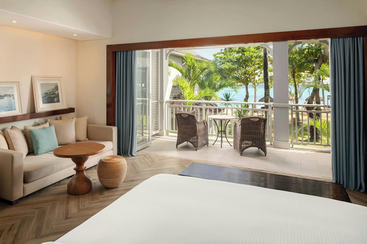 A hotel room with a balcony, a sofa, a round coffee table, and wicker chairs.