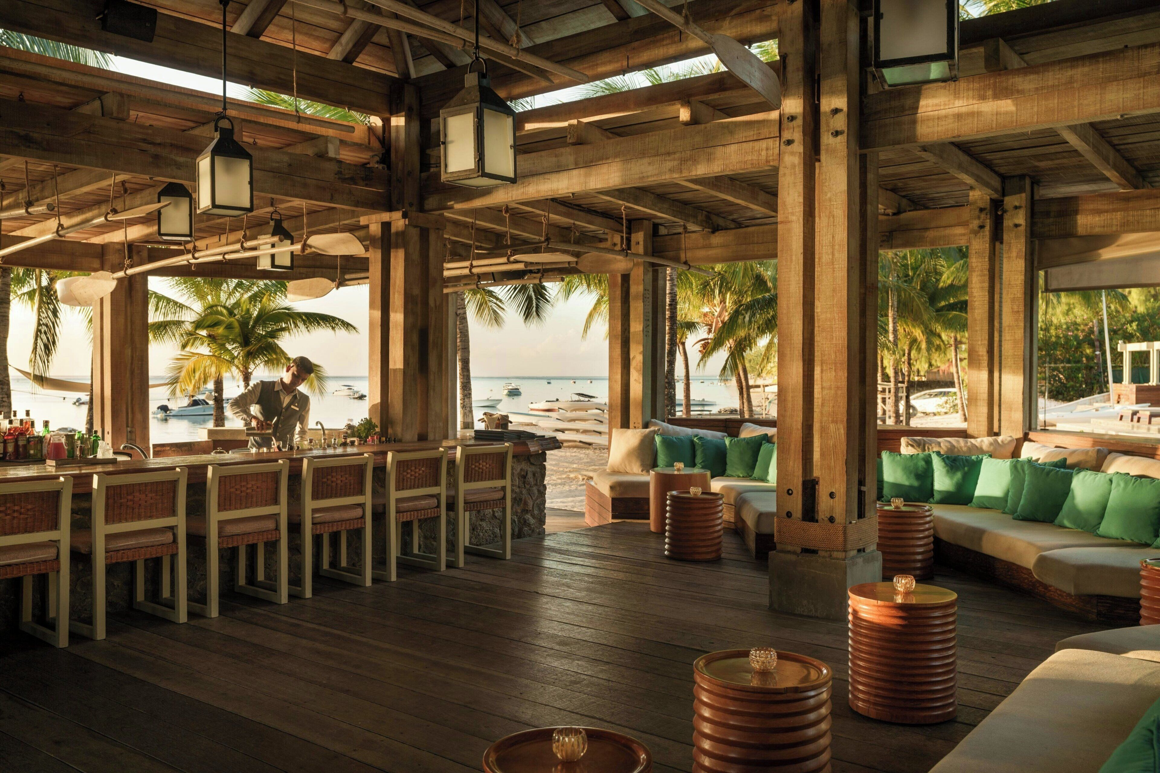 A beachside bar with wooden furniture and a view of the ocean.