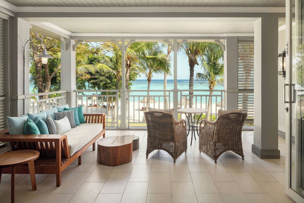 A covered outdoor seating area with a view of the ocean, furnished with a sofa, chairs, and a table.