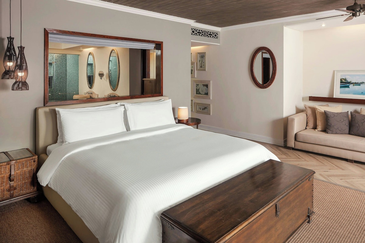 A neatly arranged bedroom with a large bed, a wooden chest, a sofa, and a wall-mounted mirror.