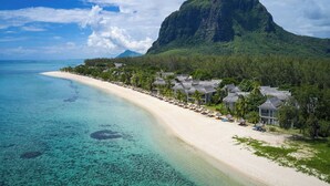 A beach resort with a long sandy beach, clear turquoise waters, and a prominent mountain in the background. - The St. Regis Le Morne Resort, Mauritius (Le Morne)